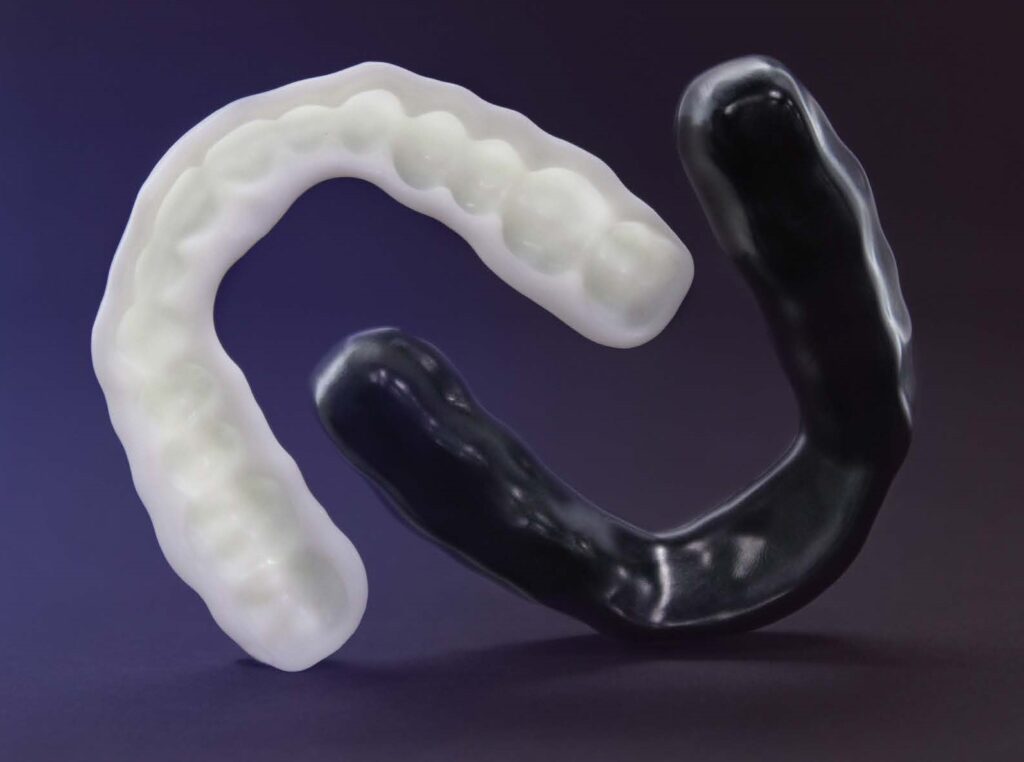 Image shows 2 athletes mouthguards in white and black that are 3d-printed with KEyGuard